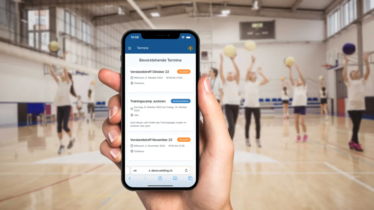 Kalender wird auf einem Smarktphone angezeigt, das in einer Sporthalle eines trainnierenden Volleyballvereins ist.